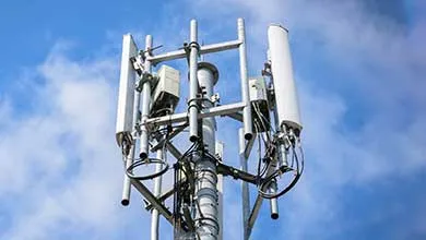 Cell phone tower top, multiple antennas, against a blue sky with white clouds.