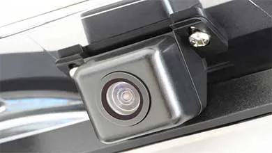 Close-up, angled view of a small, dark gray backup camera mounted on a car's exterior.