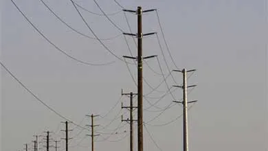 Row of wooden and metal utility poles with power lines under an overcast sky.