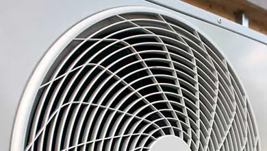 White circular fan grille on an outdoor air conditioning unit.