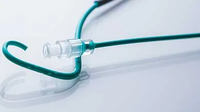 Close-up of a coiled teal medical tube with a clear plastic connector on a white reflective surface.
