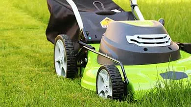 Close-up of a bright green and black lawnmower on a lush green lawn.