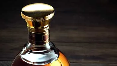 Close-up of a glass liquor bottle with a large, shiny gold cap on a dark wood background.