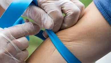 Close-up of gloved hands securing a blue tourniquet on a patient's upper arm.