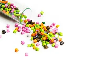 Colorful plastic pellets spilling from a clear container onto a white surface.
